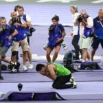 Arshad Nadeem, a Pakistani Olympian, kneeling in celebration after winning a gold medal at the 2024 Paris Olympics, surrounded by photographers capturing the moment.