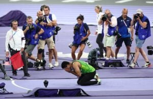 Arshad Nadeem, a Pakistani Olympian, kneeling in celebration after winning a gold medal at the 2024 Paris Olympics, surrounded by photographers capturing the moment.