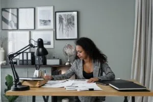 Focused businesswoman working on documents at her desk, surrounded by paperwork and modern office decor.